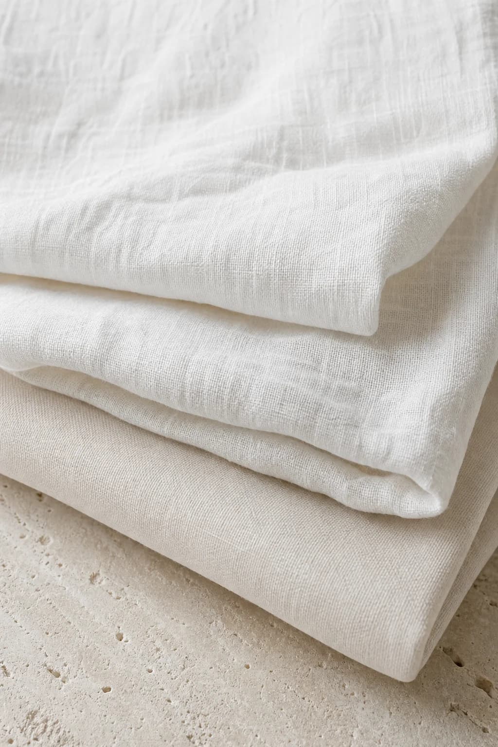 Folded white linen and cotton fabric on pale stone